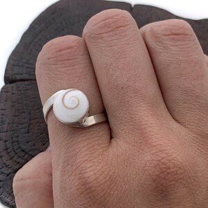 May include: A silver ring with a white shell inlay featuring a spiral pattern.