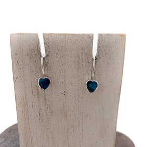 May include: A pair of silver heart-shaped earrings with blue abalone shell inlays displayed on a wooden stand.