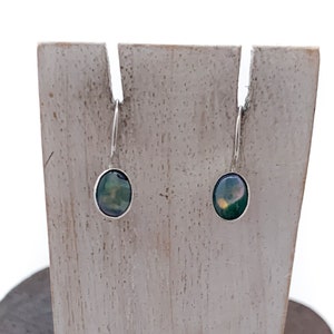 May include: A pair of silver earrings with oval-shaped green and black stones.