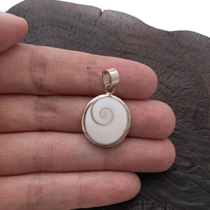 May include: A silver pendant featuring a white seashell with a spiral pattern.