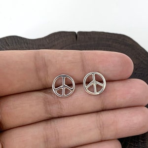 May include: A pair of silver peace sign stud earrings. The earrings are small and delicate, and they are perfect for everyday wear.