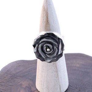 May include: A black rose ring with a silver centre, displayed on a wooden stand.