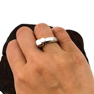 May include: A silver ring with a round, white stone set in the centre. The ring is on a person's finger.