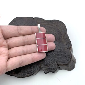 Pu&ograve; includere: Un ciondolo d'argento con tre pietre rosse rettangolari incastonate in una cornice d'argento.