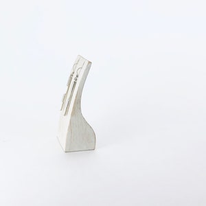 May include: A pair of silver dangle earrings with a cylindrical design displayed on a white wooden stand.