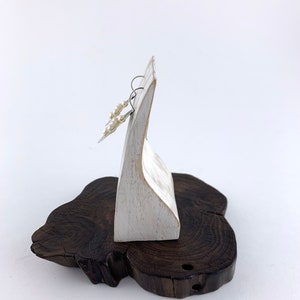 Op de afbeelding: Een paar parel oorbellen op een witte houten displaystandaard. De standaard staat op een donkerbruine houten basis.