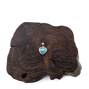 May include: A silver heart-shaped pendant with a blue and green abalone shell inlay. The pendant is displayed on a dark brown wooden surface.