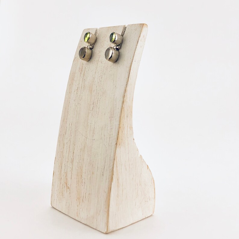 May include: A pair of silver stud earrings with green gemstones. The earrings are displayed on a white wooden stand.