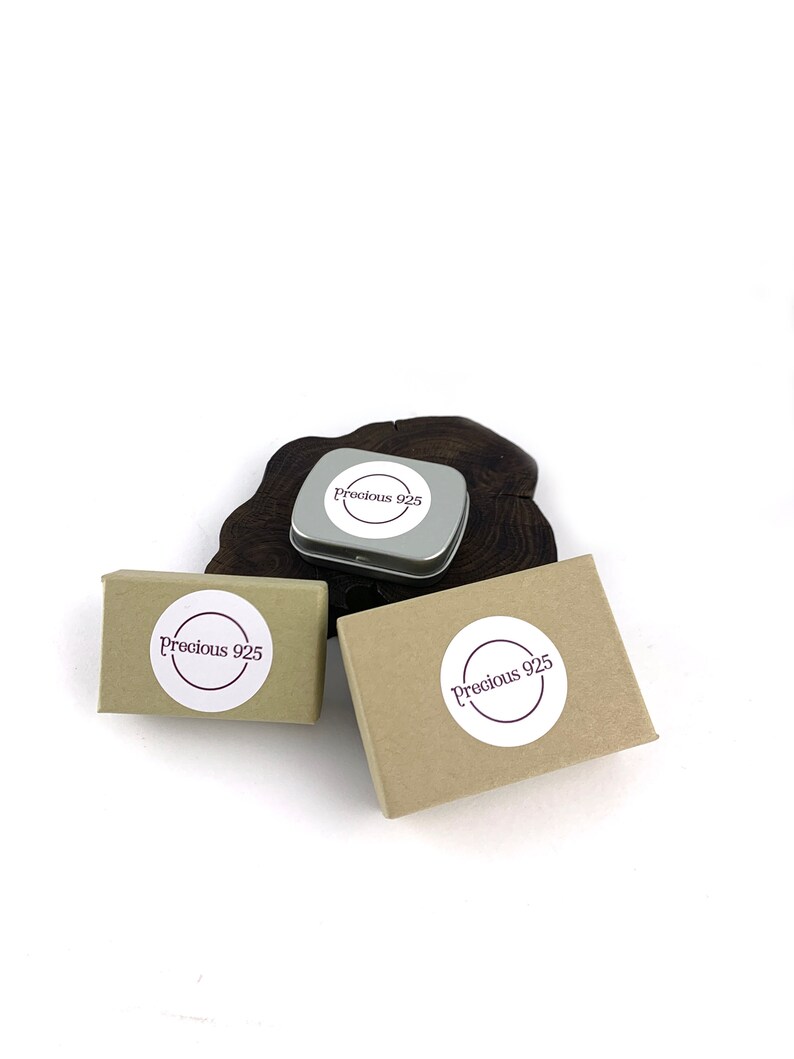 May include: Three small boxes with the text "Precious 925" on them. The boxes are brown and white and are sitting on a wooden surface.