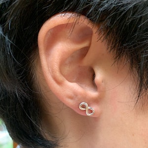 May include: A close-up of a person's ear with a silver infinity symbol earring.