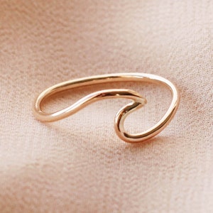 May include: A gold-coloured ring in the shape of a wave. The ring has a simple, elegant design with a smooth, polished finish. The wave design is a popular symbol of the ocean and surfing.