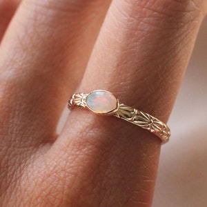 Pu&ograve; includere: Un delicato anello d'oro con una pietra di opale bianca incastonata in un design floreale.