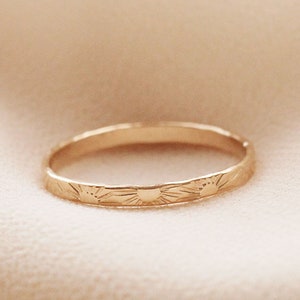 May include: A thin gold band ring with a delicate sunburst design.