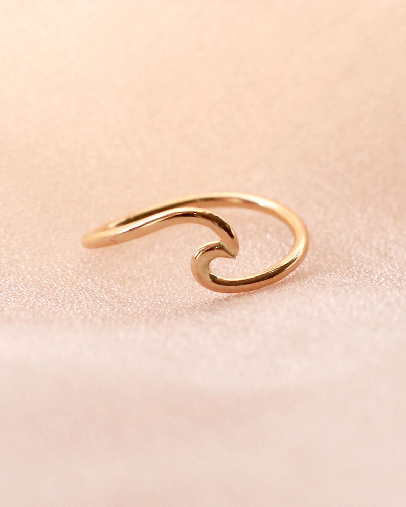 May include: A gold-coloured ring shaped like a wave. The ring has a simple, elegant design with a smooth, polished finish. The wave design is a popular symbol of the ocean and surfing.