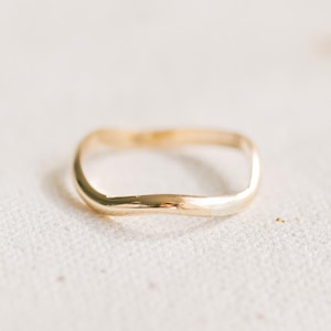 May include: A gold-colored ring with a unique, wavy design. The ring has a smooth, polished surface and a slightly irregular shape, adding to its handcrafted appeal. The ring is a piece of jewelry.