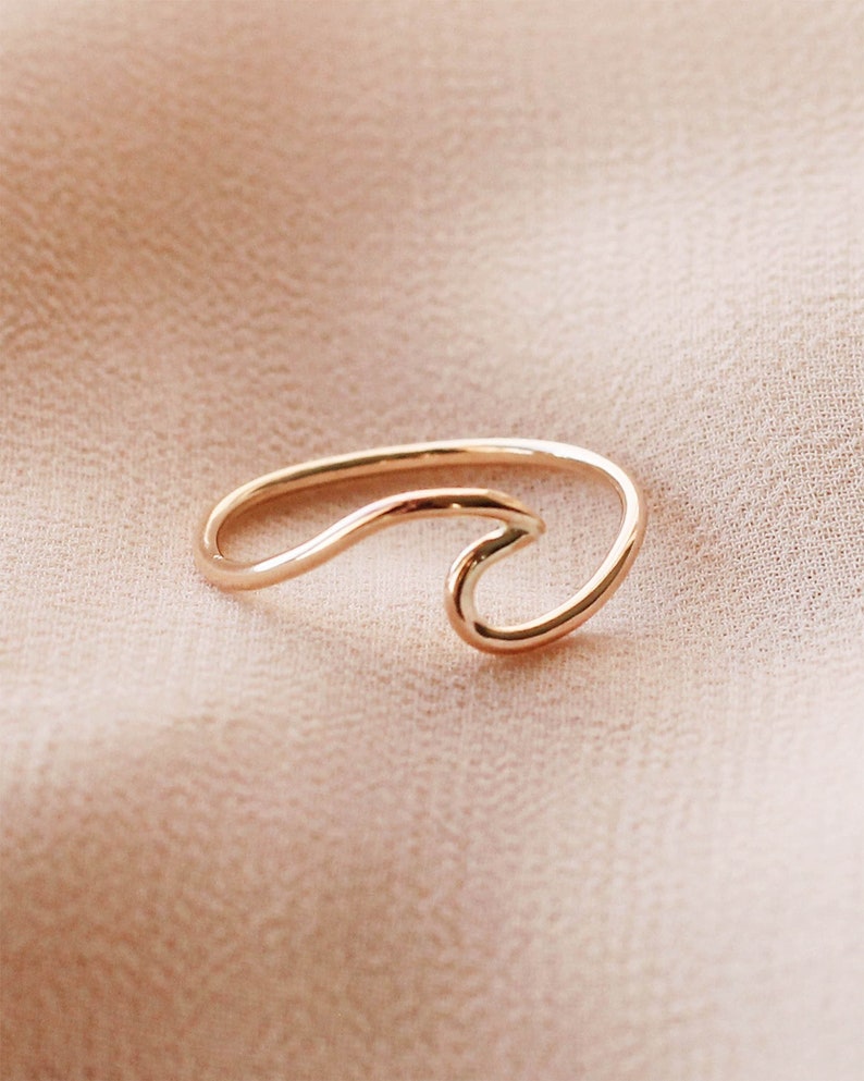 May include: A gold-coloured ring in the shape of a wave. The ring has a simple, elegant design with a smooth, polished finish. The wave design is a popular symbol of the ocean and surfing.
