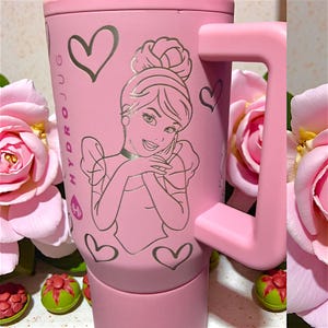 May include: Pink travel mug with a silver outline of a princess and hearts. The mug has a large handle and the words "HYDRO JUG" are printed on the side. The mug is surrounded by pink roses.