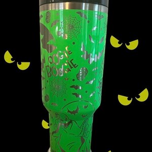 Puede incluir: Un vaso de acero inoxidable verde con un dise&ntilde;o plateado de murci&eacute;lagos, telara&ntilde;as y las palabras "Oogie Boogie".