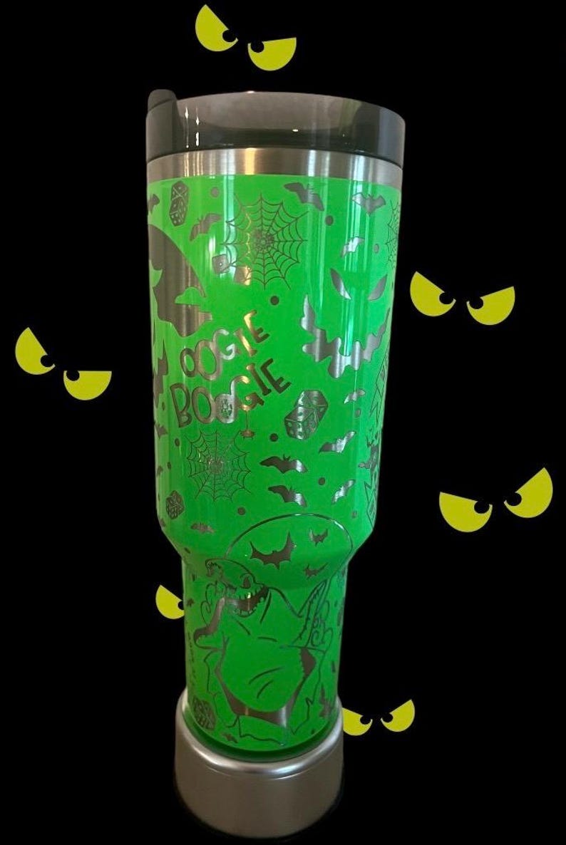 Puede incluir: Un vaso de acero inoxidable verde con un dise&ntilde;o plateado de murci&eacute;lagos, telara&ntilde;as y las palabras "Oogie Boogie".