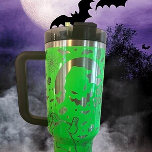 Puede incluir: Taza de viaje de acero inoxidable verde con asa y tapa negras. La taza presenta una silueta blanca de Jack Skellington de Pesadilla antes de Navidad, murci&eacute;lagos y las palabras "This is Halloween".