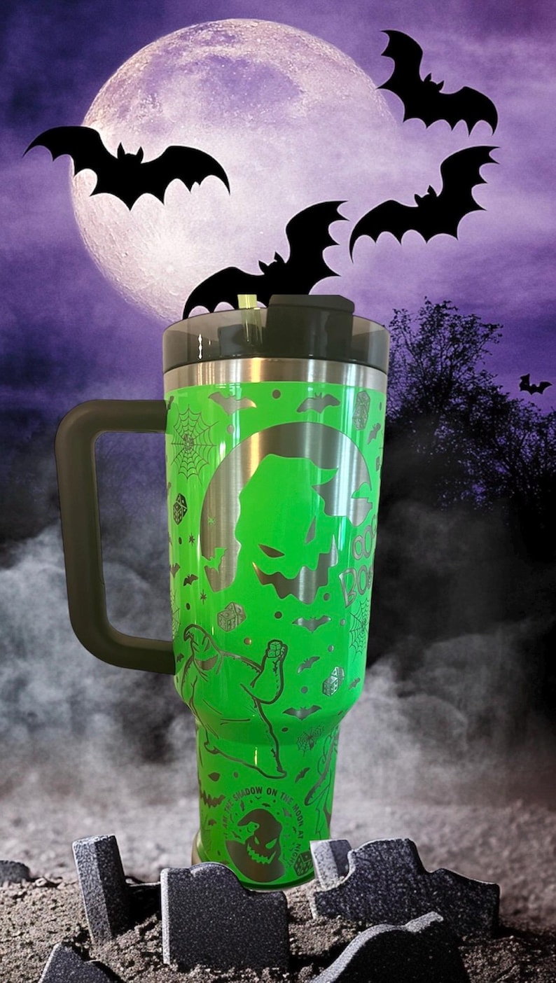 Puede incluir: Taza de viaje de acero inoxidable verde con asa y tapa negras. La taza presenta una silueta blanca de Jack Skellington de Pesadilla antes de Navidad, murci&eacute;lagos y las palabras "This is Halloween".