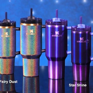 May include: A collection of Stanley tumblers and mugs in various sizes and finishes. The tumblers feature iridescent "Fairy Dust" and deep purple "Star Shine" designs. Each has a lid and the Stanley logo.