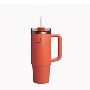 Puede incluir: Una taza de viaje de acero inoxidable de color coral con asa y una pajita. La taza tiene una tapa con un agujero para pajita integrado y el logotipo de Stanley est&aacute; impreso en el lateral.