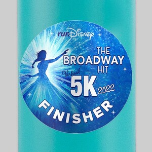 May include: A turquoise water bottle with a black lid and handle. The bottle has a sticker on it that says "runDisney The Broadway Hit Virtual 5K 2022 Finisher".