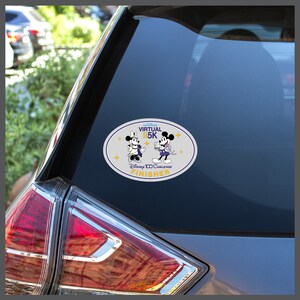May include: A white oval sticker with a gray background featuring Mickey Mouse and Minnie Mouse dressed in purple and white outfits. The sticker says "Virtual 5K Disney 100 Challenge Finisher".