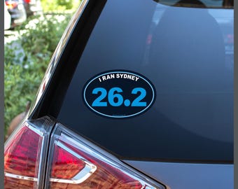 May include: A blue and black oval sticker with the text "I ran Sydney 26.2" on a car window.