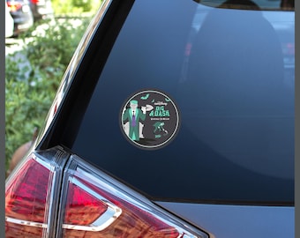 May include: A circular sticker on a car window featuring a cartoon character in a green suit holding a shovel. The text reads "runDisney DIG & DASH VIRTUAL 5K-10K 2024". The design includes a tombstone, small green bats, and a smaller figure running.