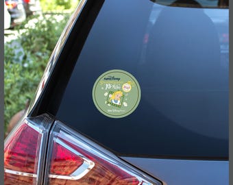May include: A circular sage green sticker applied to a car window featuring the text runDisney Springtime Surprise 10-Miler 2027, an illustration of Alice from Alice in Wonderland, a gold pocket watch, and small white flower accents.