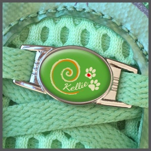 May include: A green shoe lace charm with a swirl design and paw prints. The charm has the name "Kellie" written on it.