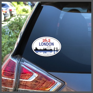 May include: A white oval sticker with a blue and black silhouette of the London skyline, including the London Eye and Tower Bridge. The text "26.2 LONDON" is printed in red and black.