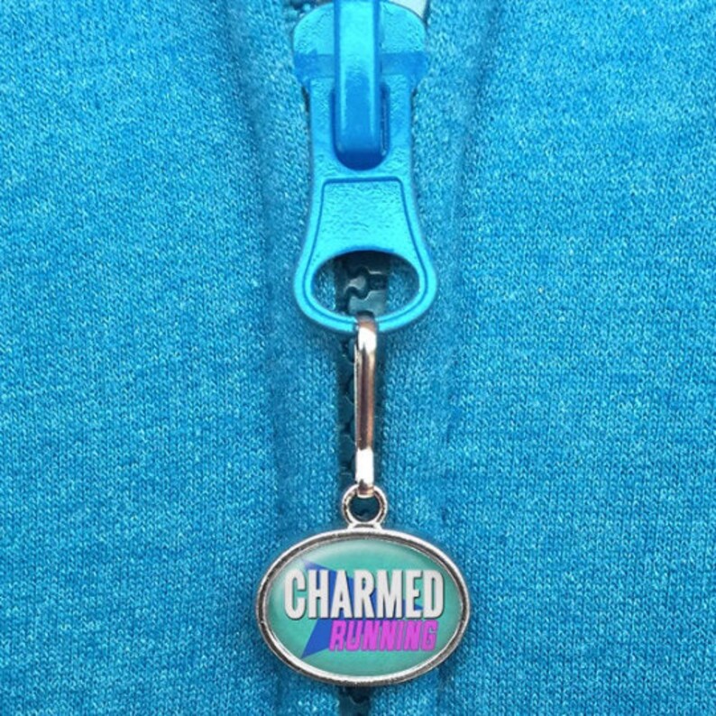 May include: A silver zipper pull with a blue oval charm that says "CHARMED RUNNING" in pink and white letters on a teal background.
