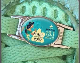 May include: A silver-toned oval shoe lace charm featuring a teal background with an illustration of Princess Jasmine, a palace silhouette, and text that reads Disney Princess Half Marathon 13.1 Miles 2027, attached to light green shoelaces.