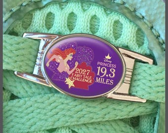 May include: A silver-toned oval shoe lace charm featuring a purple background with an illustration of a red-haired character, a yellow starfish, and text that reads 2027 FAIRY TALE CHALLENGE DISNEY PRINCESS 19.3 MILES, attached to light green laces.