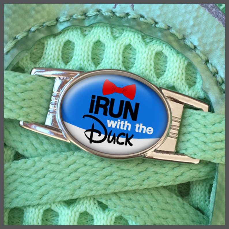 May include: A silver shoe lace charm with a blue and white oval design. The charm features a red bow and the text "iRUN with the Duck".
