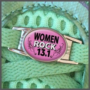 Peut inclure: Un charm de chaussure argenté avec un centre ovale rose. Le centre porte les mots "WOMEN ROCK 13.1" en noir. Le charm est sur un lacet vert, avec un fond en maille verte. Le charm est conçu pour les coureurs.