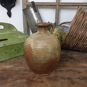 Peut inclure: Un pichet en céramique rustique de couleur brune avec une anse. Le pichet a une surface texturée et est légèrement verni.