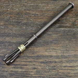 Peut inclure: Un outil en métal noir avec une bande dorée et une extrémité pointue. L'outil est conçu pour retirer de petits objets des espaces restreints.