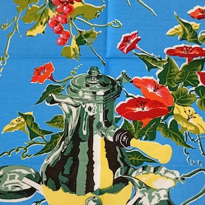 May include: Blue cotton tea towel with a vibrant print. The design includes a bunch of red grapes, red and yellow flowers, and a silver teapot and creamer. Two glasses of red wine are also shown.