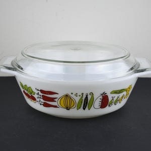 May include: White casserole dish with a clear glass lid. The dish has a colourful border of illustrated vegetables, including red peppers, onions, and tomatoes. The dish has two handles and is suitable for serving.