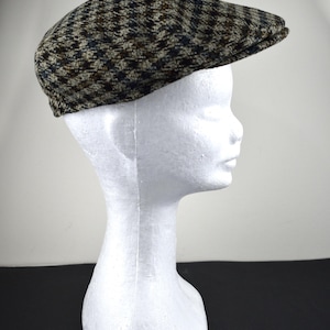 May include: A tweed newsboy cap with a classic houndstooth pattern in shades of brown, blue, and tan. The cap is displayed on a white mannequin head, showcasing its shape and design. A stylish accessory.
