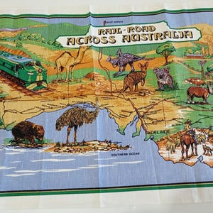 May include: A colorful map of Australia with a green train, camel, kangaroo, and other animals. The text "RAIL-ROAD ACROSS AUSTRALIA" is displayed across the top. The map is hand printed.