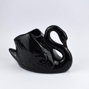 May include: A glossy black swan-shaped ceramic planter. The swan has a curved neck and a wide opening for plants or flowers. The planter is a decorative item for home decor.