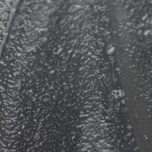 May include: A dark gray, textured surface with a bumpy, uneven finish. The material appears to have a slightly glossy or wet sheen, with small, irregular protrusions scattered across the entire area, creating a tactile and rugged visual appearance.