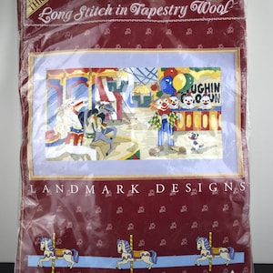 May include: A tapestry wool long stitch kit featuring a carnival scene with a clown, carousel, and the text "Laughin' Clown." The kit is packaged in a burgundy plastic with the text "Landmark Designs" and "The Carnival."