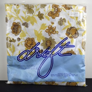 May include: A package of two flat sheets measuring 152 x 228 cm, featuring a white background with a floral pattern in shades of yellow and brown. The plastic packaging displays the brand name drift, the text finest quality cotton sheets, and washing instructions.