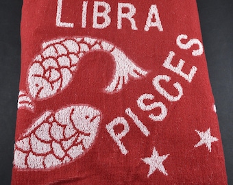 May include: A red rectangular towel featuring white woven graphics and text. The design includes the words LIBRA and PISCES, two fish symbols, a scale icon, and several star shapes. The fabric has a textured, looped pile surface throughout.